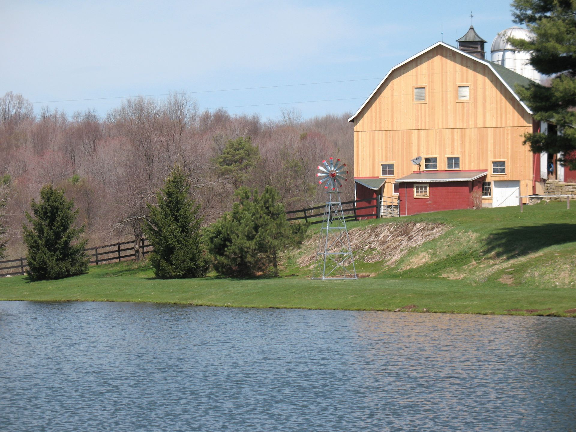Yellow barn and red shed beside a pond and trees.