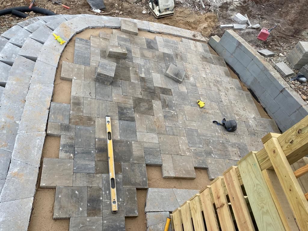 A brick walkway is being built next to a wooden fence.
