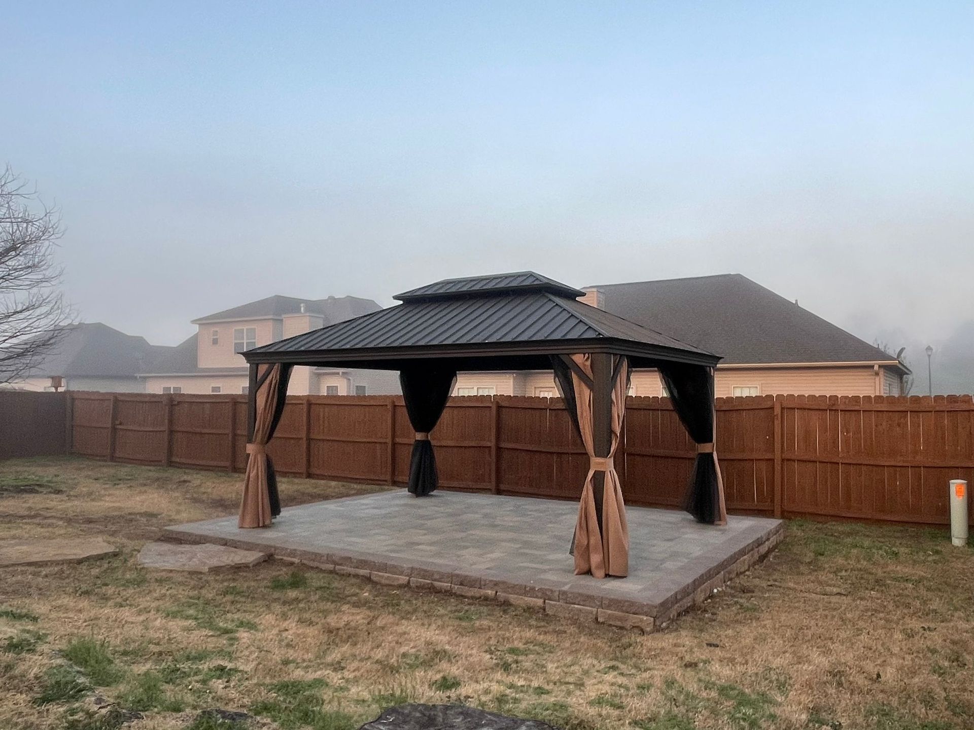 A gazebo in the backyard of a house with a wooden fence.