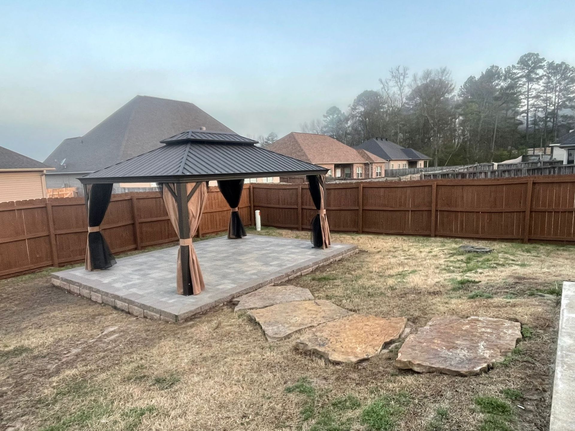 A gazebo is sitting in the middle of a backyard next to a wooden fence.