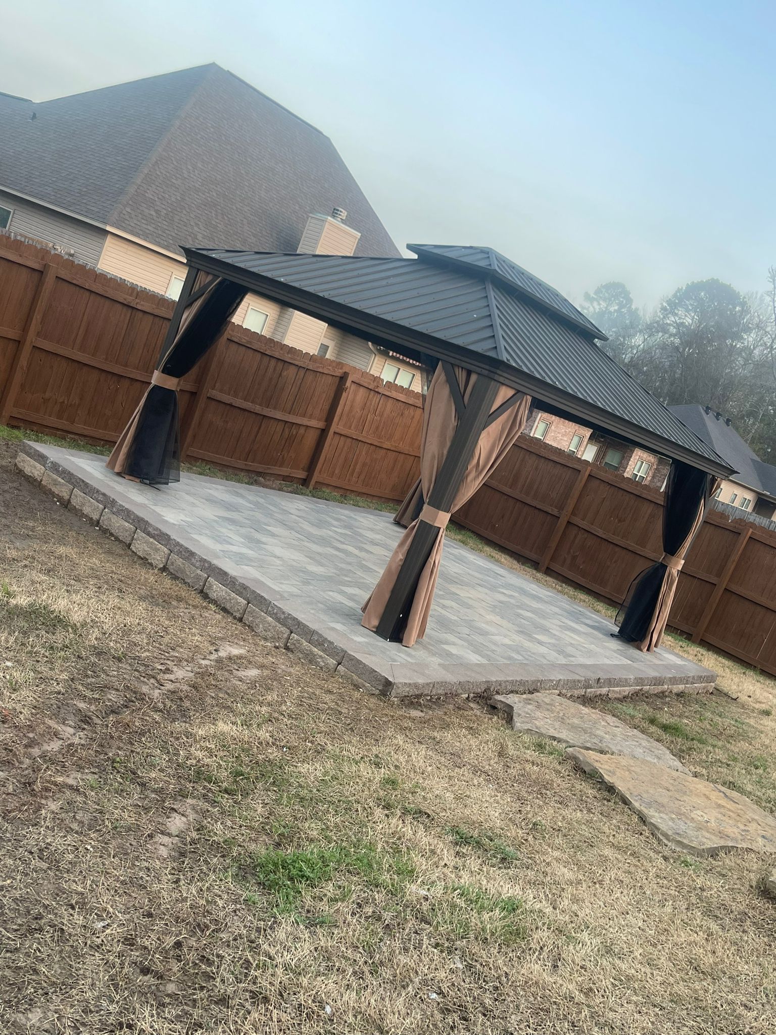 A gazebo is sitting in the middle of a backyard next to a wooden fence.