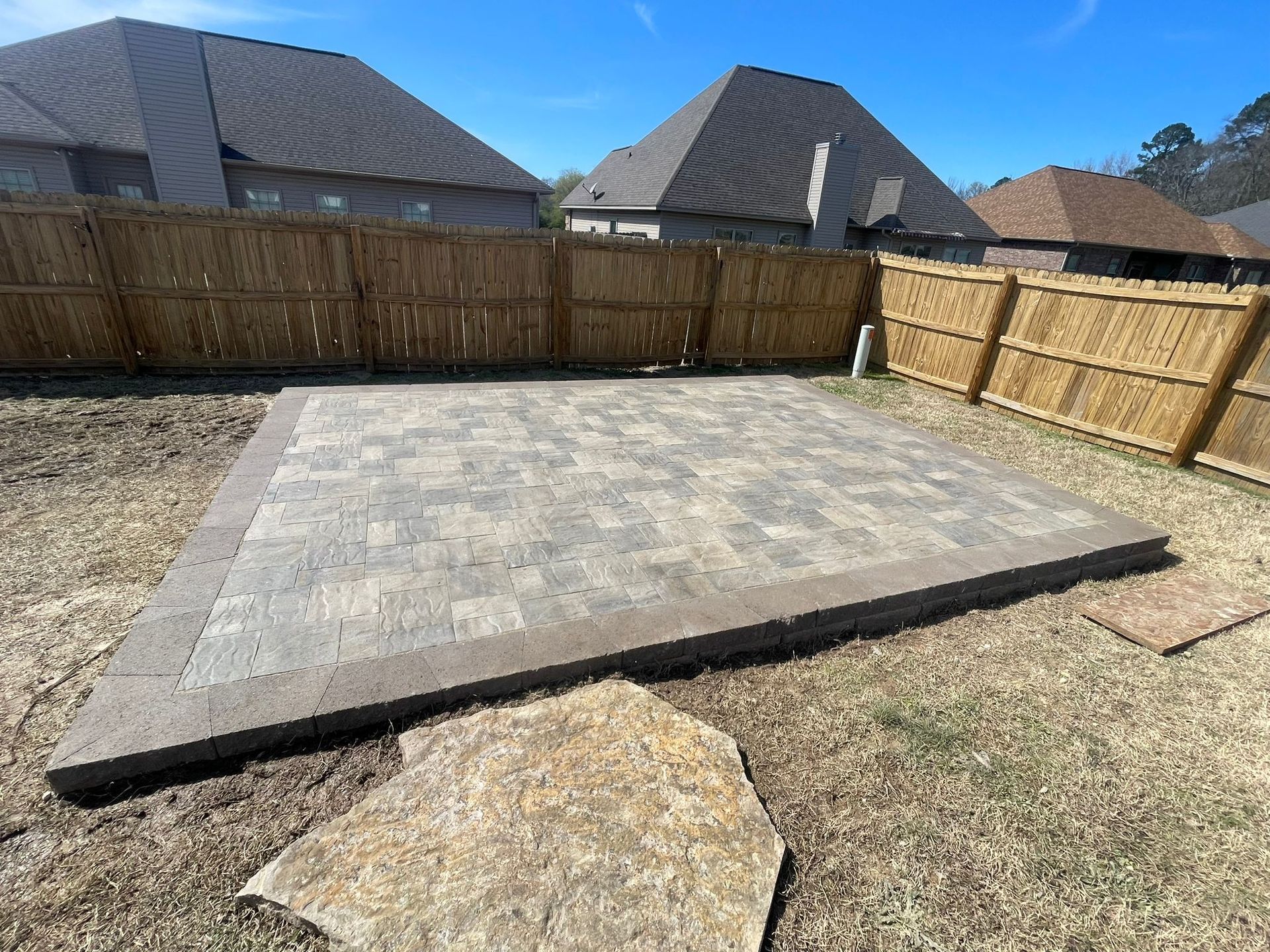 A brick patio with a wooden fence in the backyard of a house.