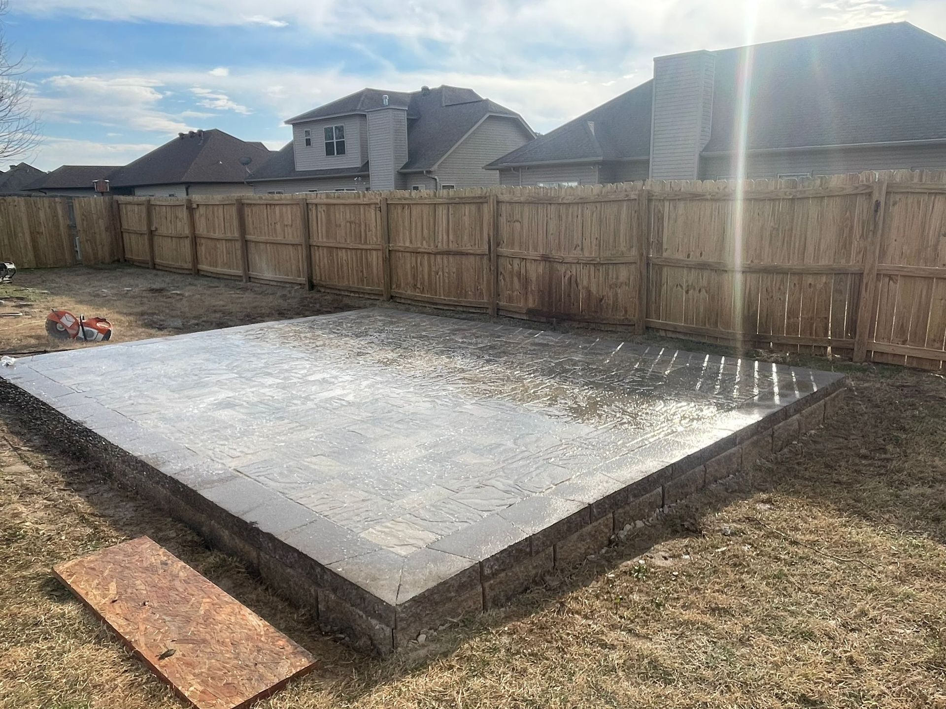 A concrete slab is sitting in the middle of a backyard next to a wooden fence.