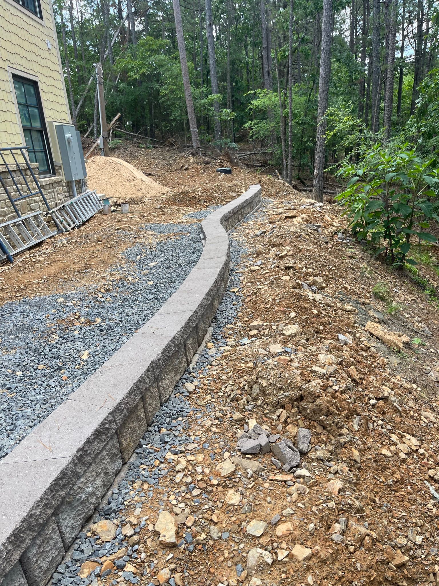 A concrete wall is surrounded by gravel and rocks in a yard.