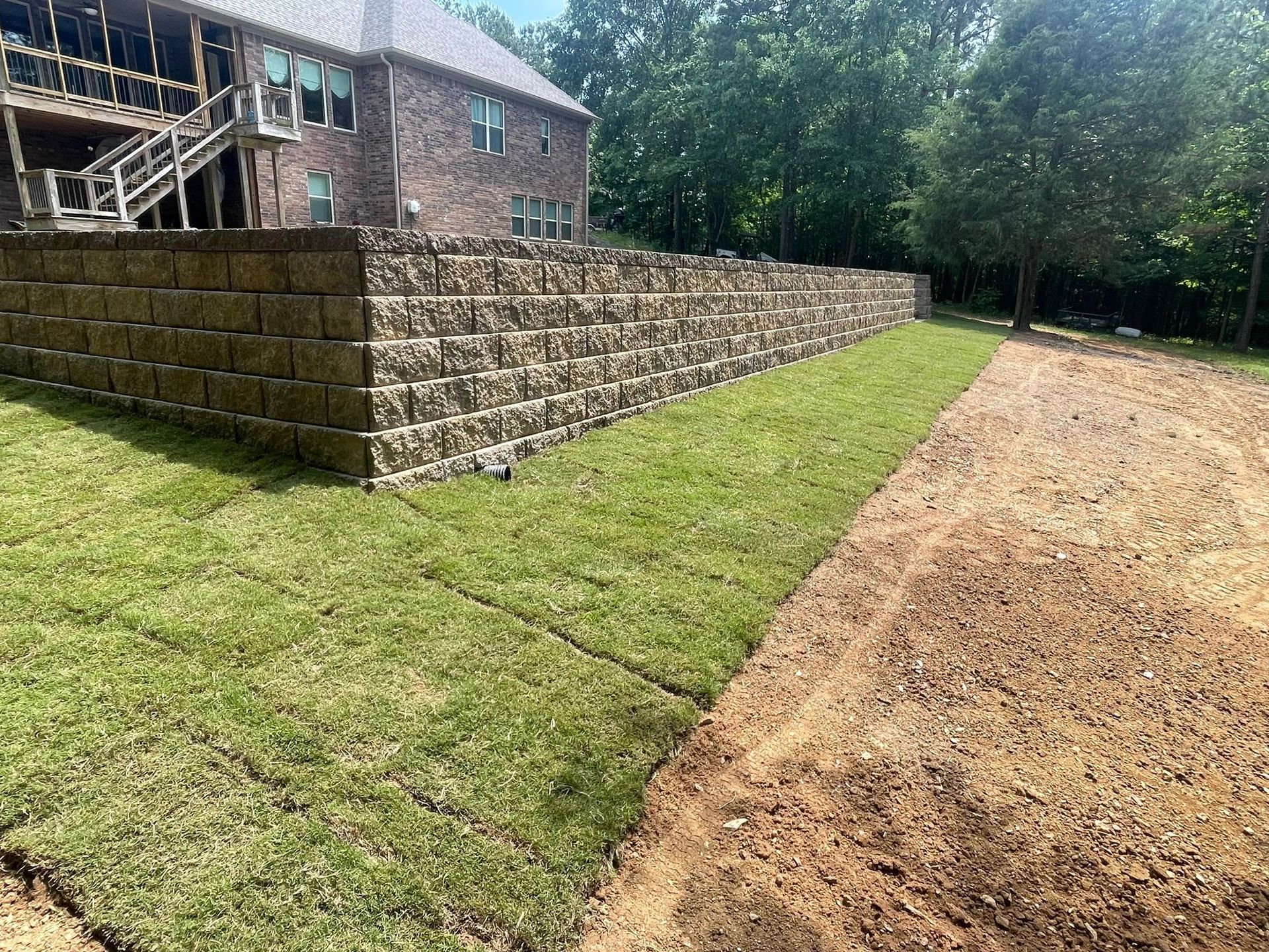 A brick wall surrounds a lush green lawn in front of a house.