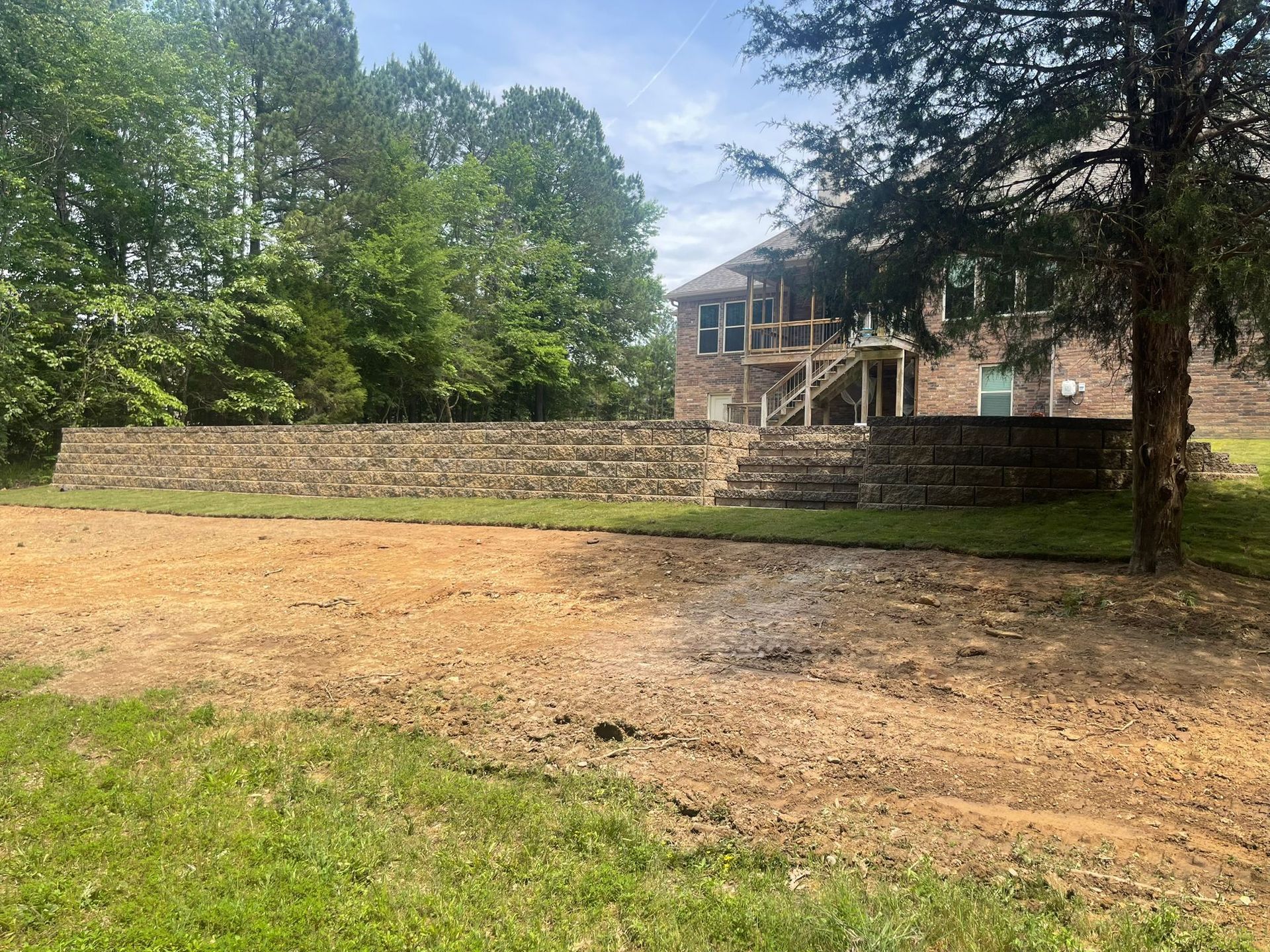 A large brick house is sitting on top of a dirt field surrounded by trees.