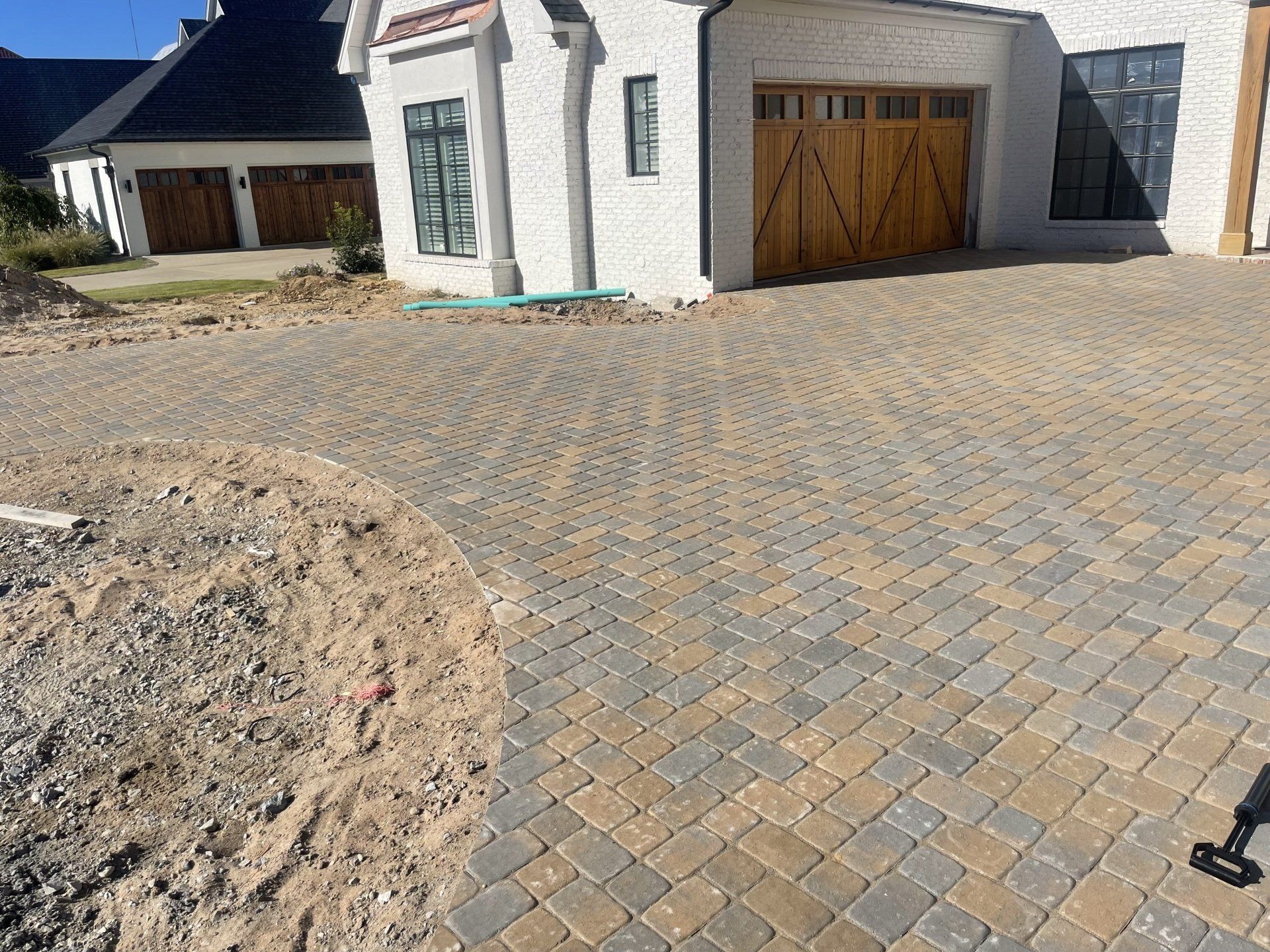 A brick driveway in front of a white house with a wooden garage door.