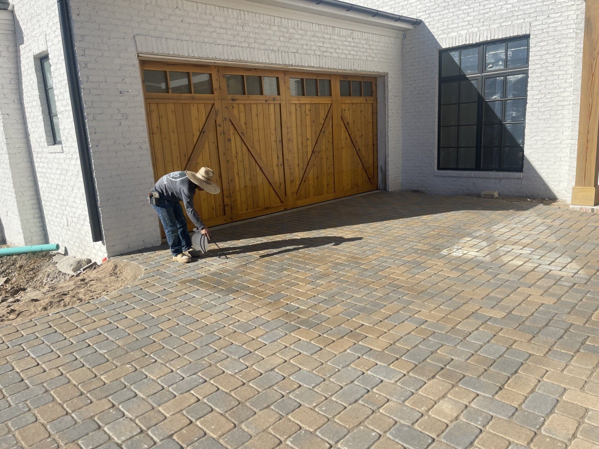 A man is standing on a brick driveway in front of a garage door.
