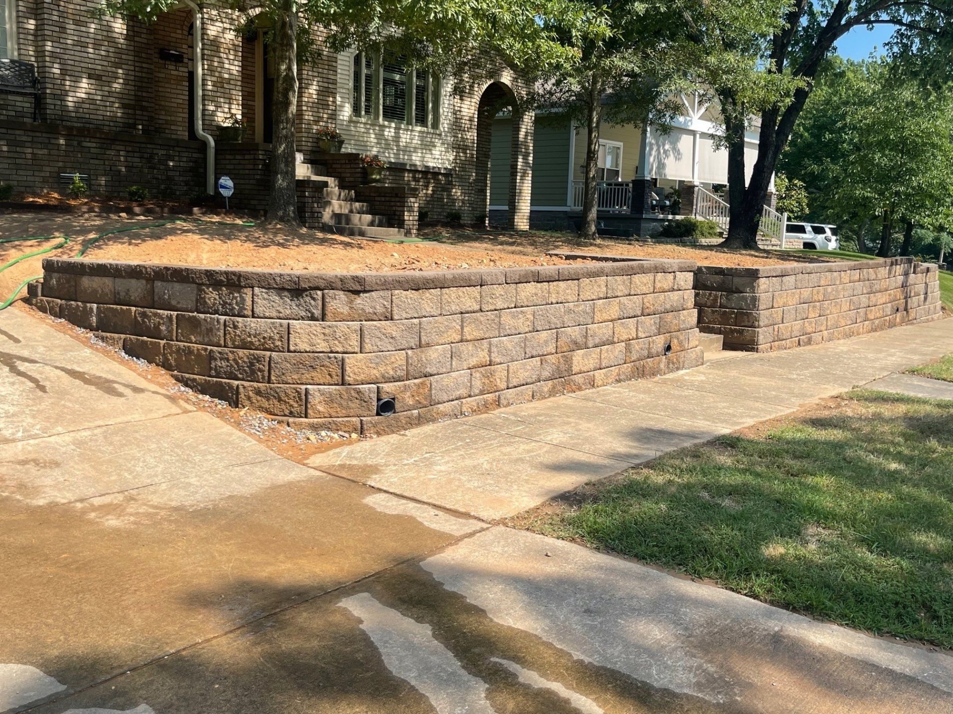 A brick wall is sitting next to a sidewalk in front of a house.