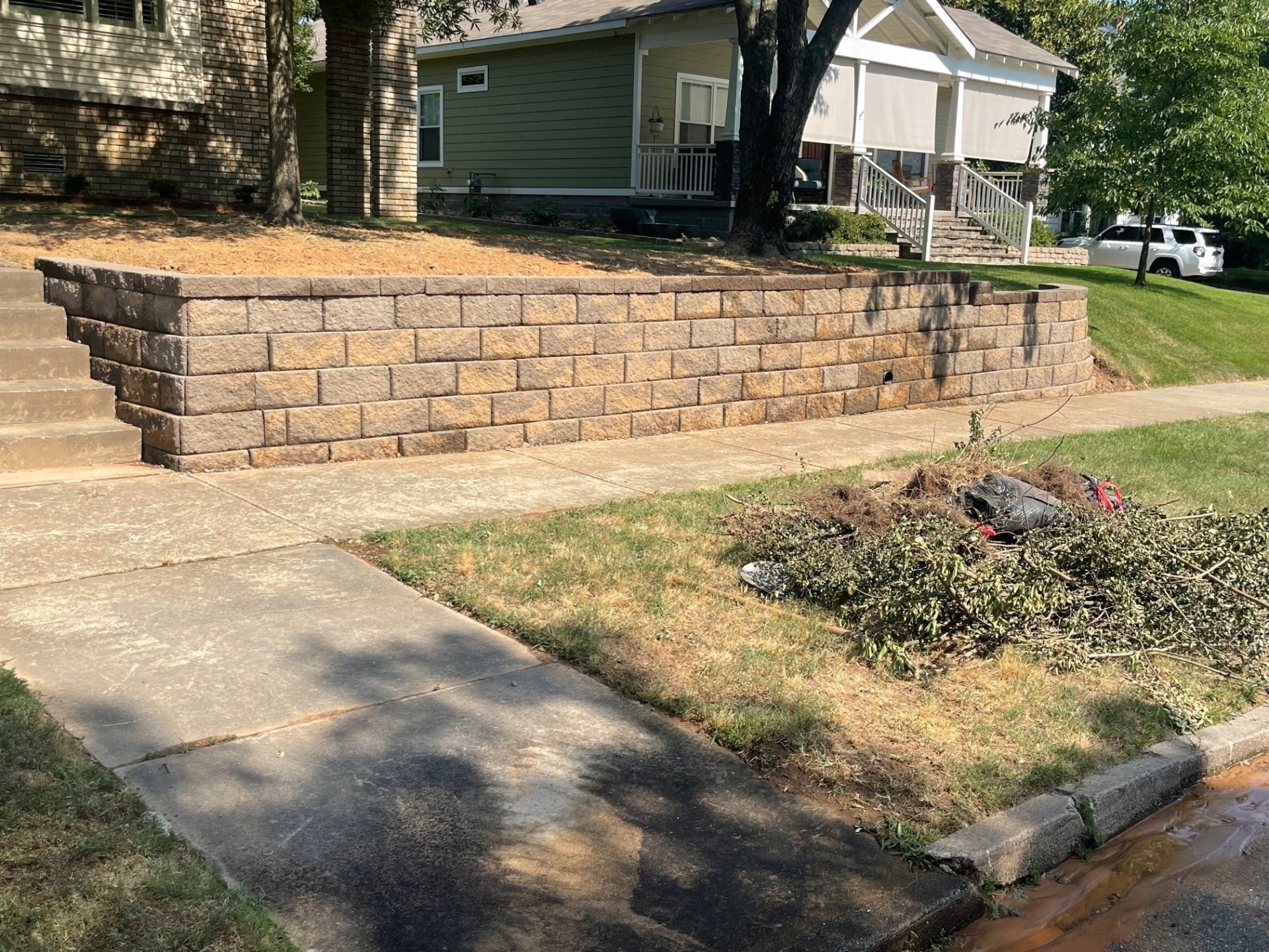 A brick wall is sitting next to a sidewalk in front of a house.