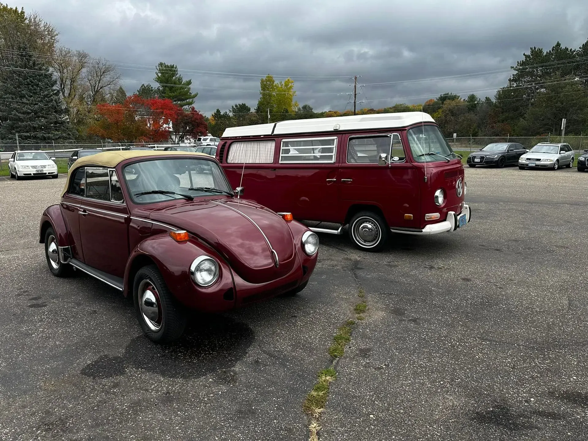 Burgundy VW Beetle convertible and van parked in a lot under cloudy skies.