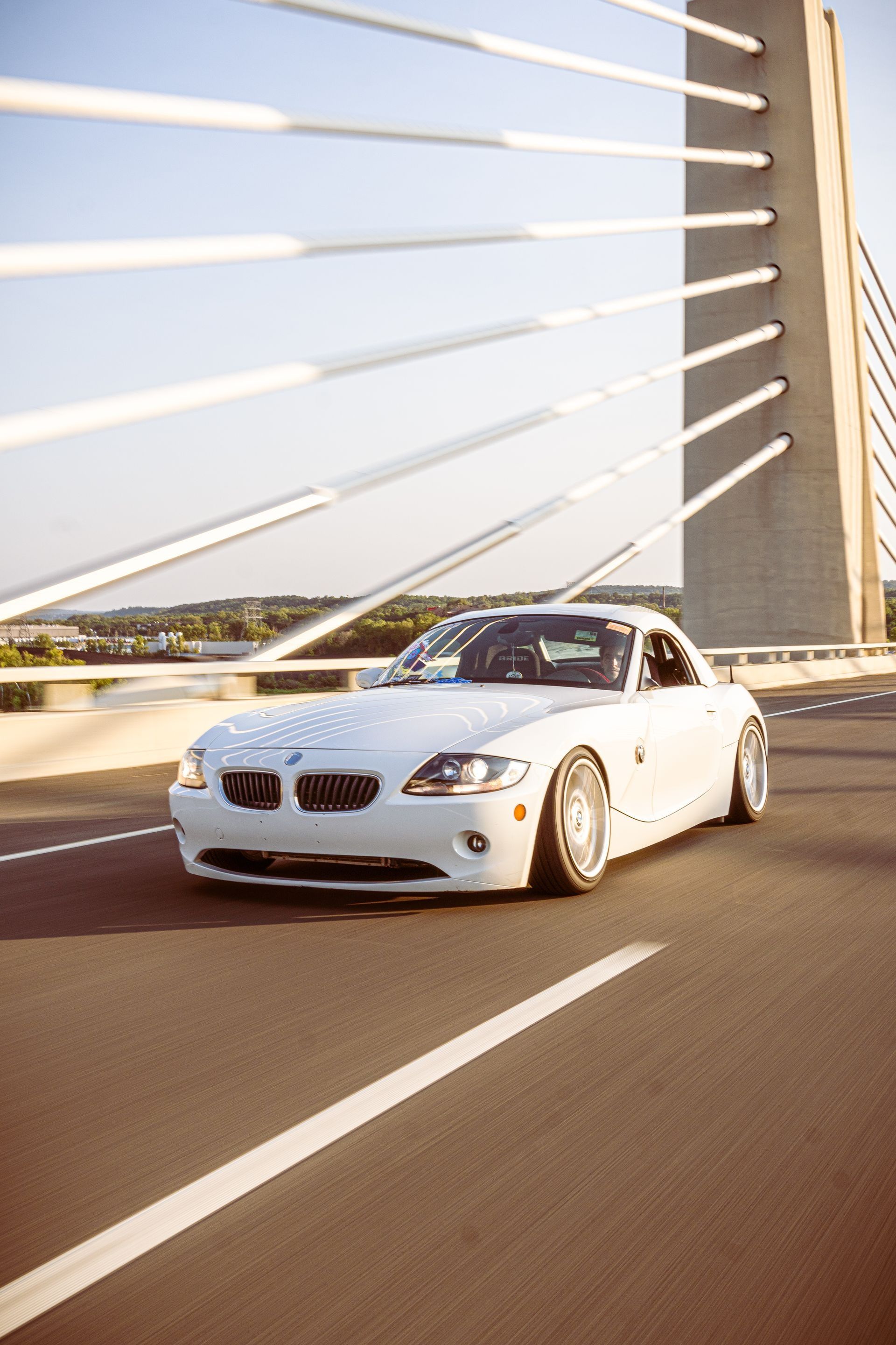 White BMW Z4 coupe driving on a bridge with a modern cable-stayed pylon.