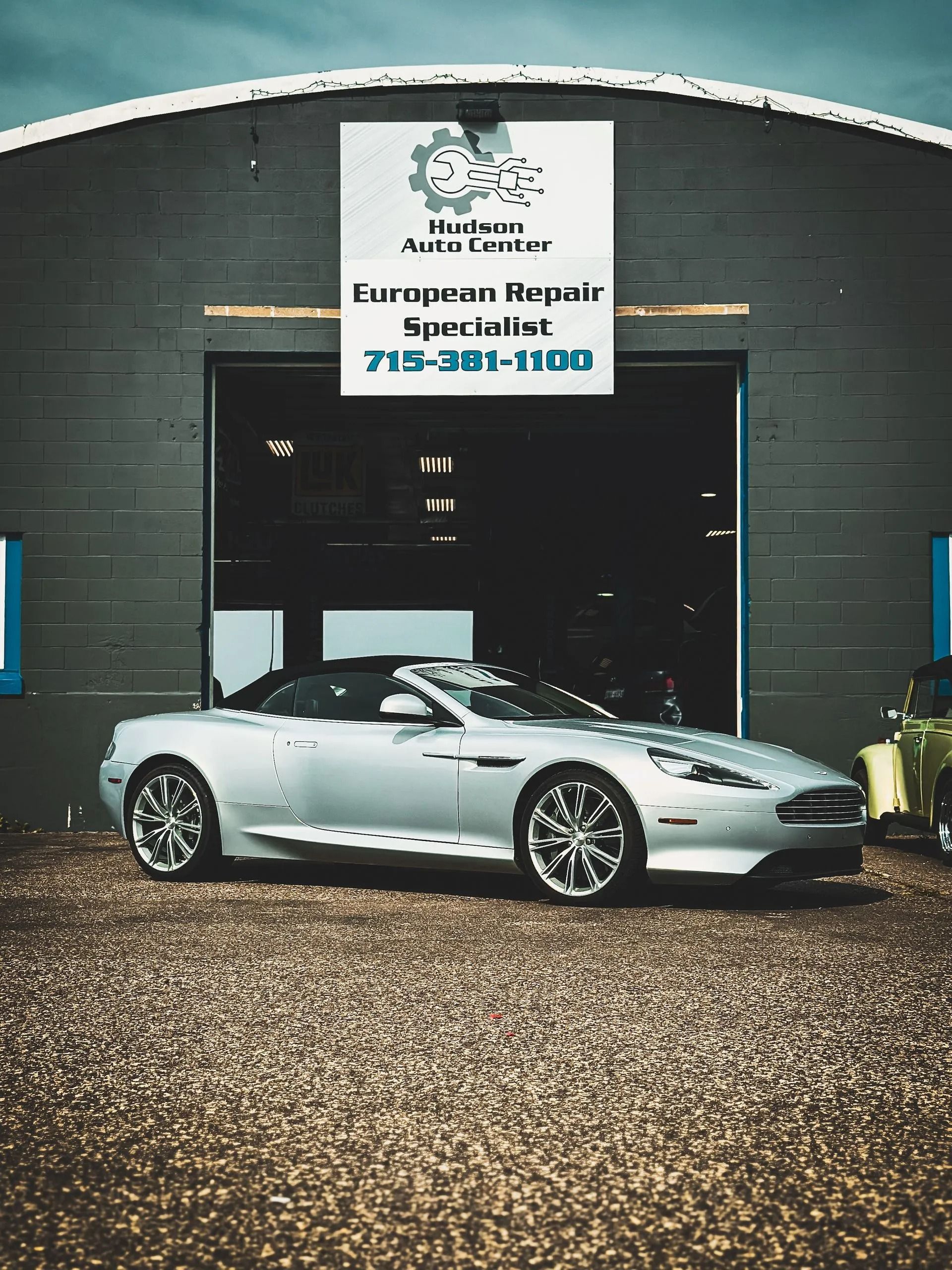 Silver convertible sports car in front of a garage with a sign for European auto repair.