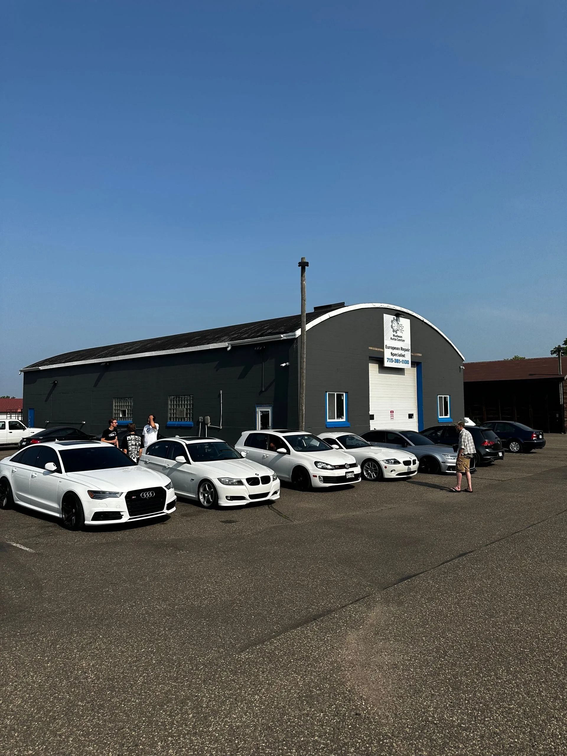 Cars parked in front of a dark grey building on a sunny day.