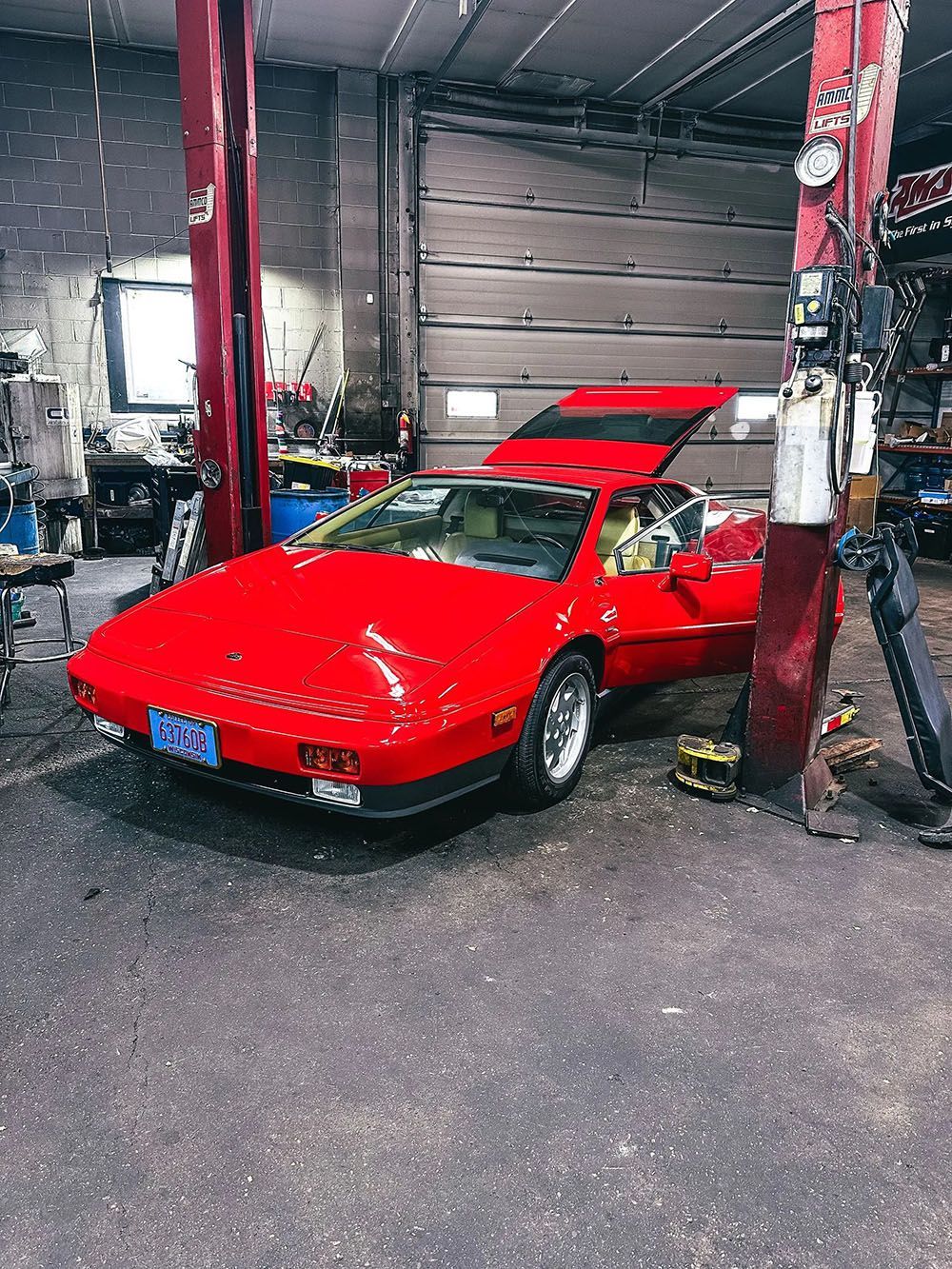 Red Lotus sports car in a garage, with its door and rear hatch open.