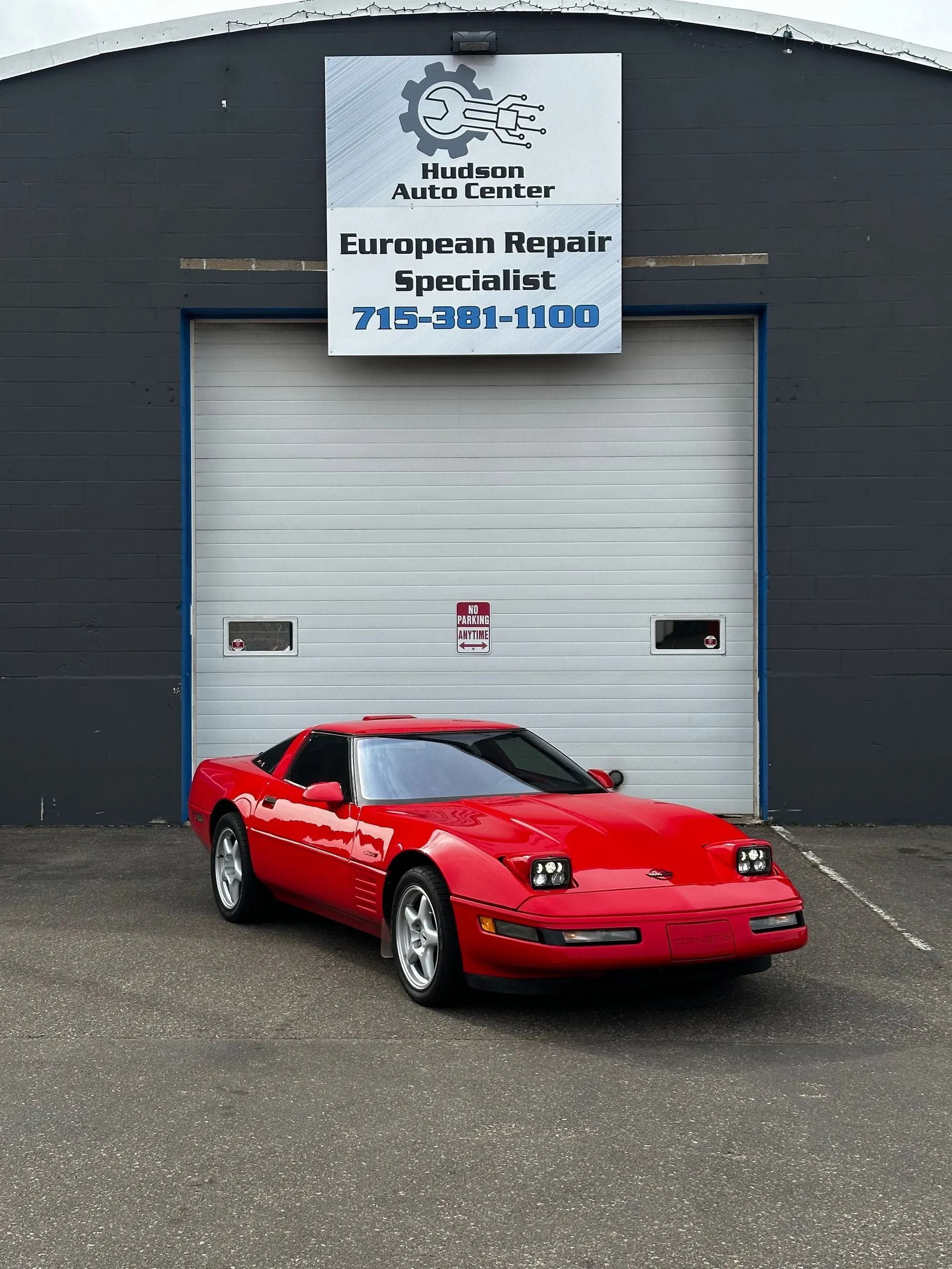 Red sports car parked in front of a garage door with a sign for European car repair.
