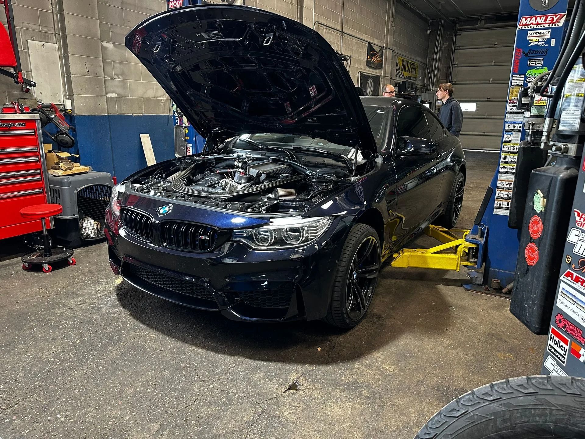 Dark blue BMW M4 with hood open, in a garage on a lift.
