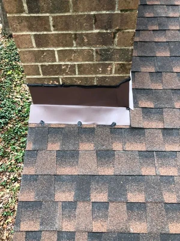 Brick chimney with brown metal flashing and asphalt shingles.