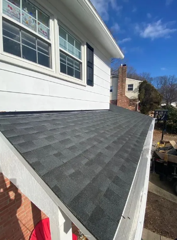 View of a newly shingled roof with white trim and a white house, against a blue sky.