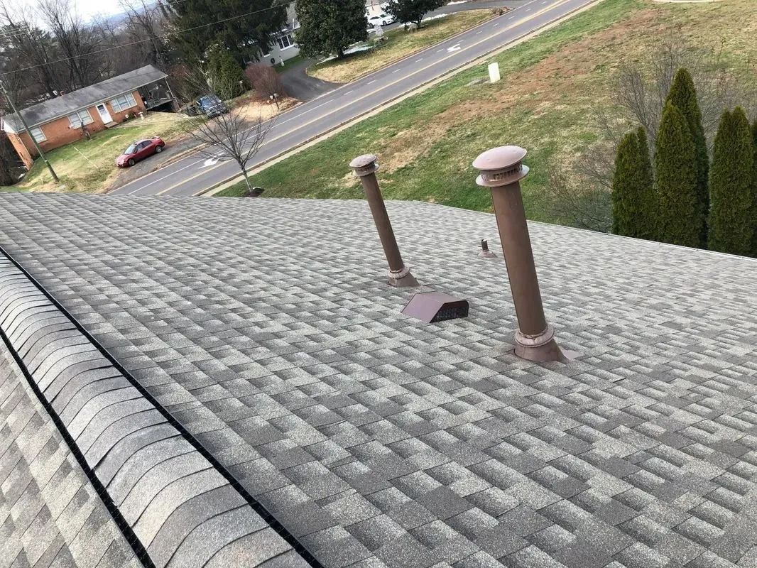 View of a gray shingled roof with three brown pipes; road and trees in background.