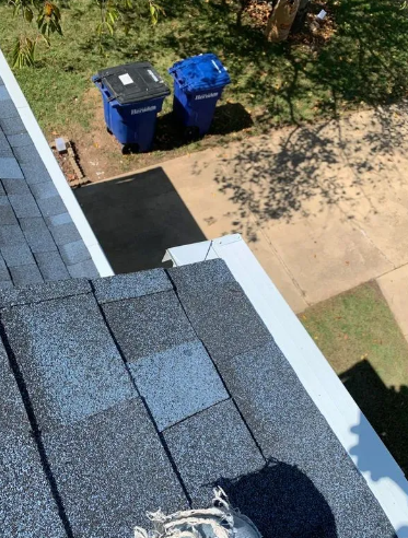 View from roof of blue and black trash bins on driveway. Blue roof shingles and white gutter.