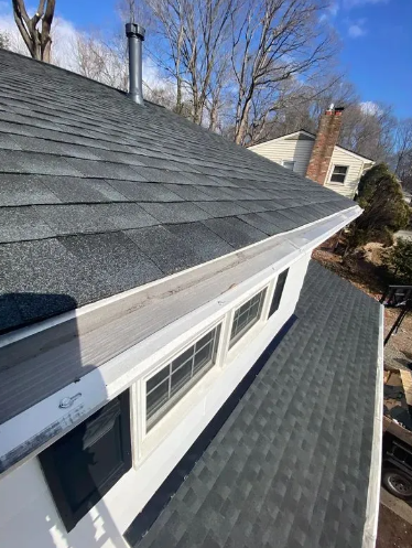 Exterior view of a house roof with gutters and windows, under a blue sky.