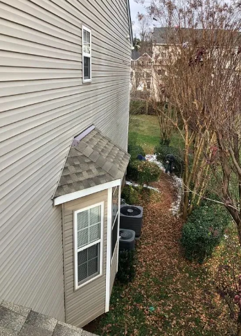 Side view of a house with light tan siding, a windowed alcove, and a small yard with fall foliage.