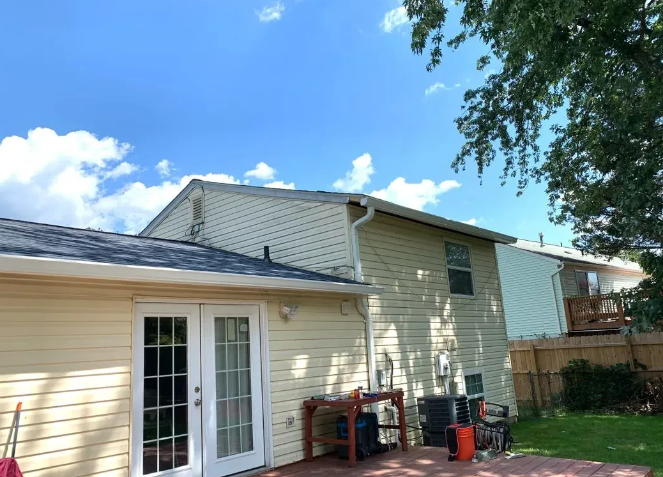 Backyard view of a two-story home with light siding and a sunny sky.