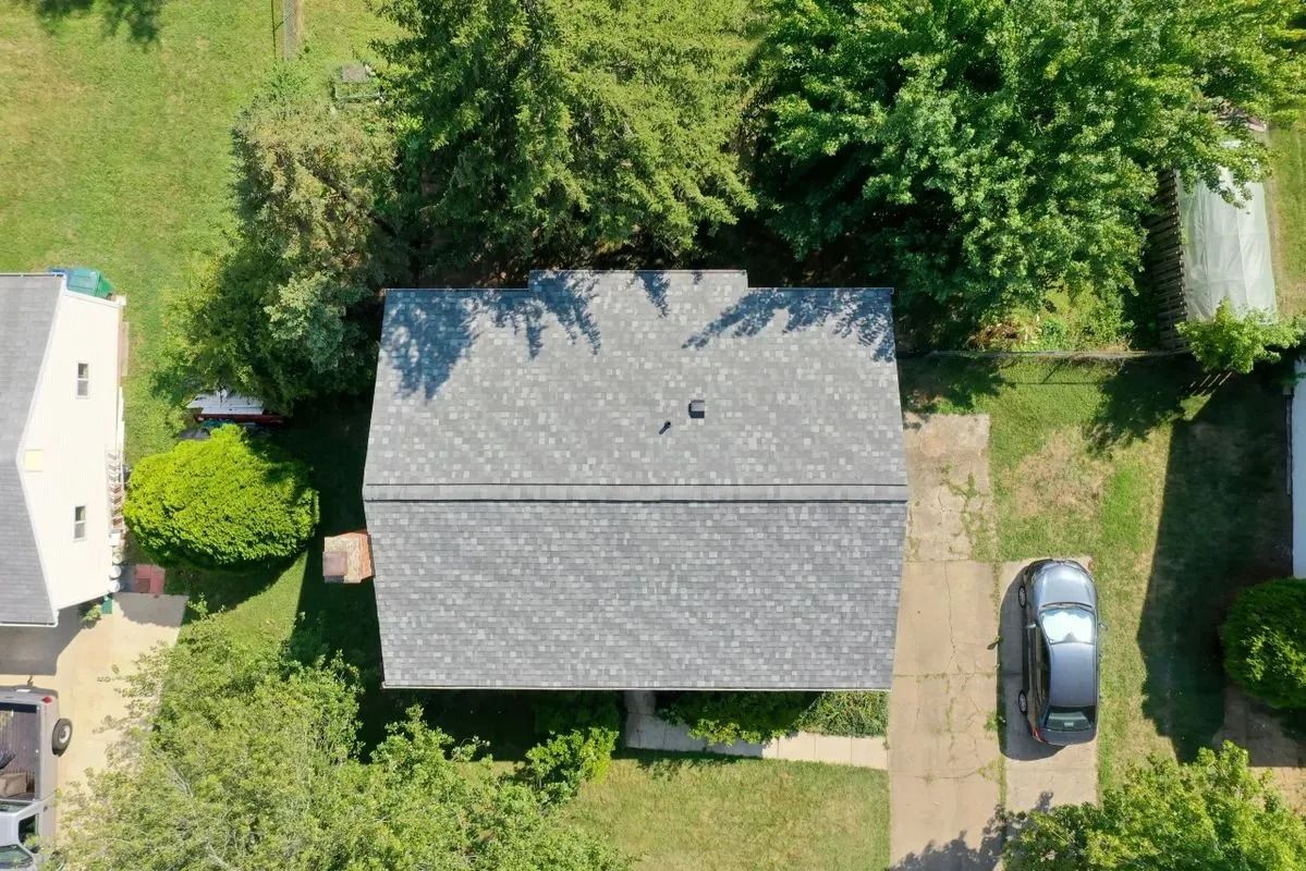 Overhead view of a house with a gray roof, surrounded by trees and a driveway with a car.