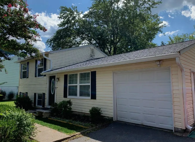 Yellow house with black shutters, a garage, and a green yard under a cloudy sky.