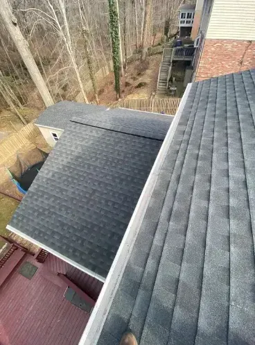 View of rooftops with gray shingles, gutters, and a backyard with trees.