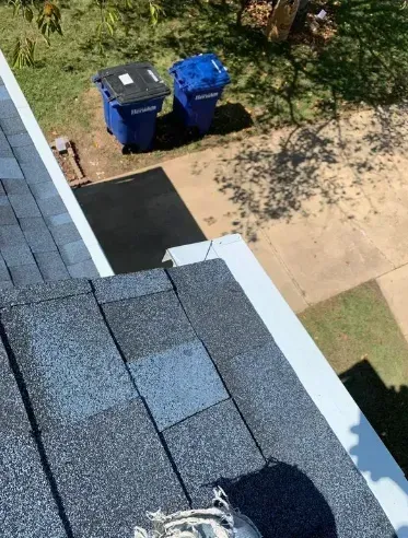 View from roof of blue and black trash bins on driveway. Blue roof shingles and white gutter.