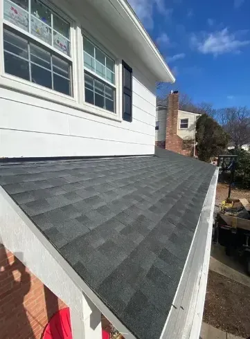 View of a newly shingled roof with white trim and a white house, against a blue sky.