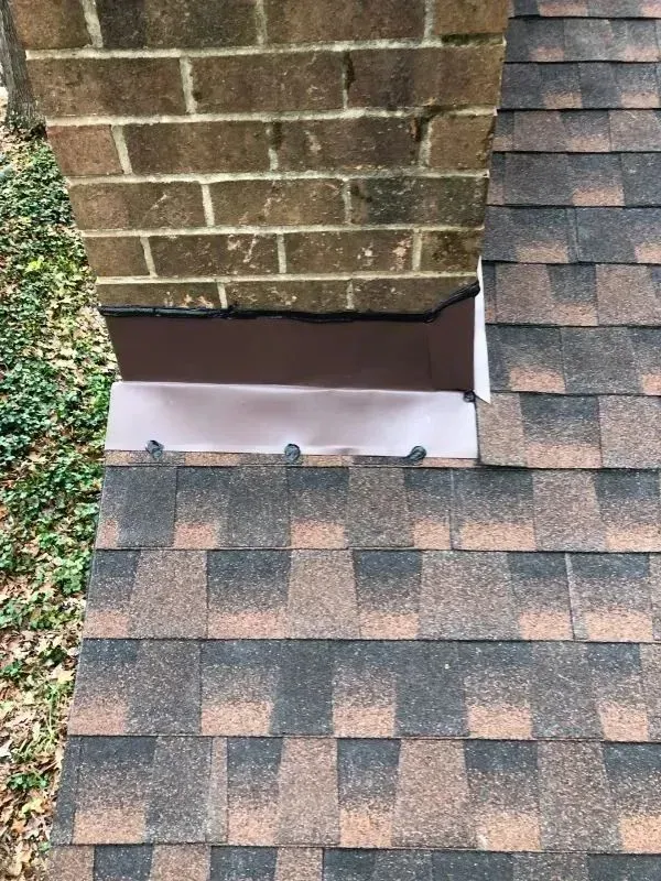 Brick chimney with brown metal flashing and asphalt shingles.
