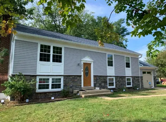Light blue siding home with dark gray roof, light brown door, and stone facade.