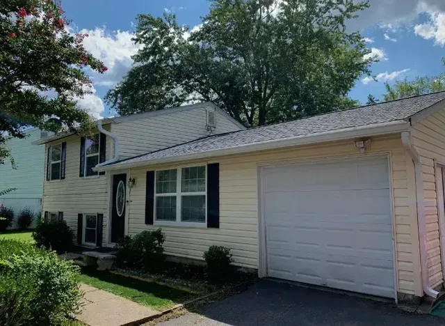 Yellow house with black shutters, a garage, and a green yard under a cloudy sky.