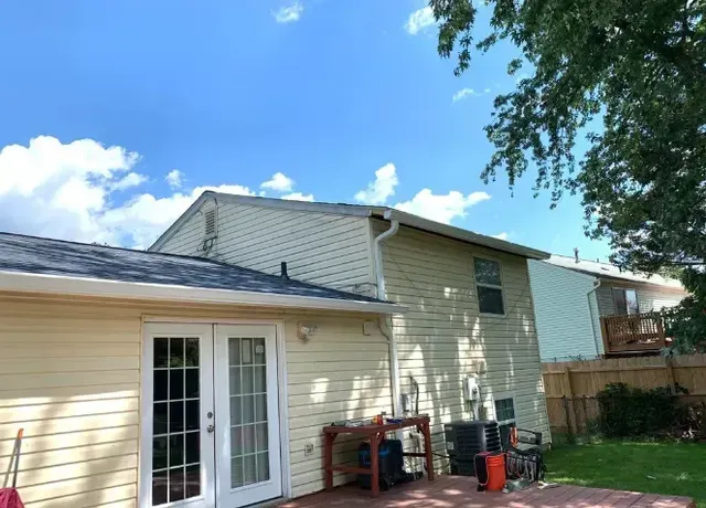 Backyard view of a two-story home with light siding and a sunny sky.