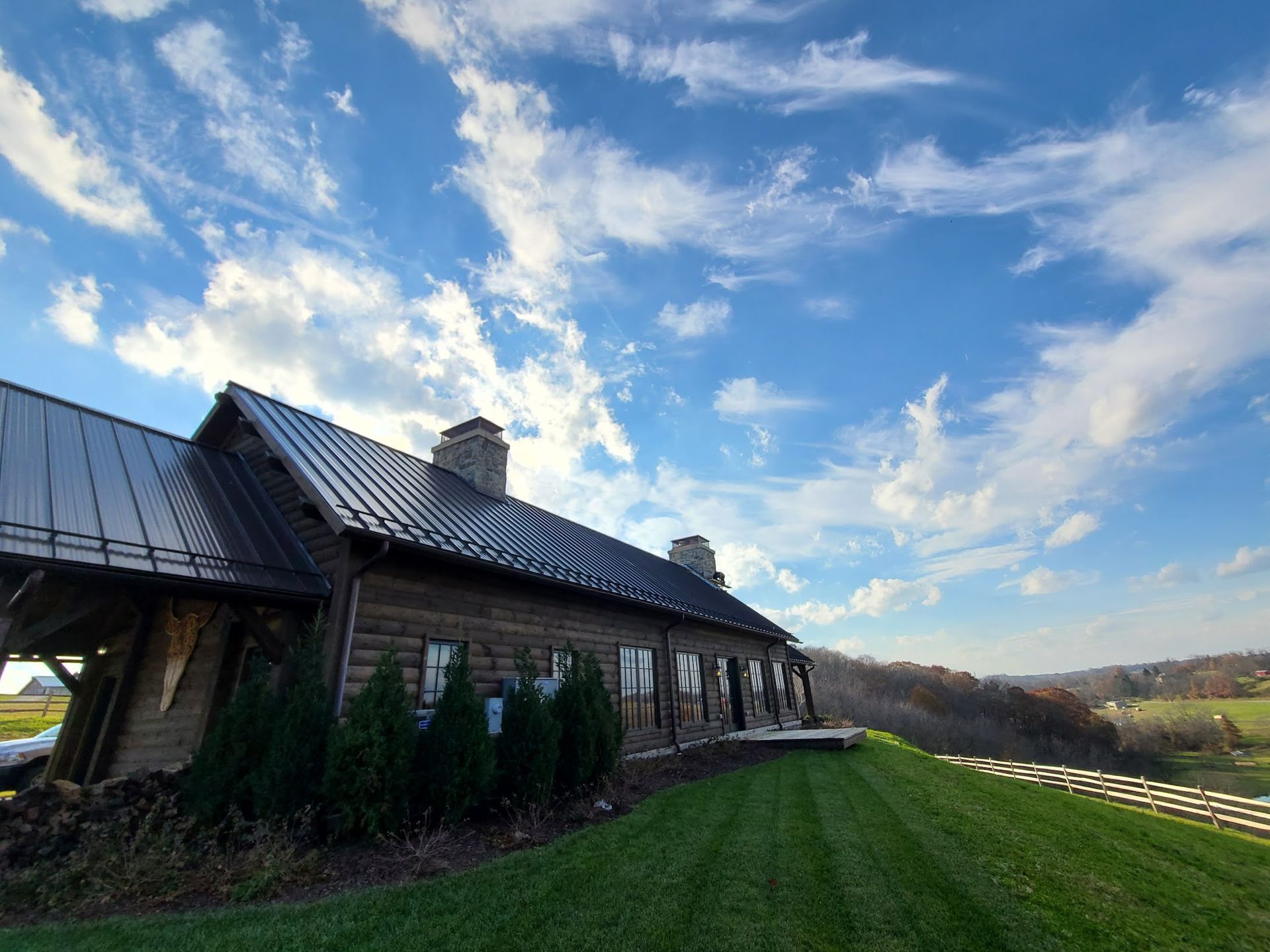 A large house with a metal roof is sitting on top of a lush green hillside.