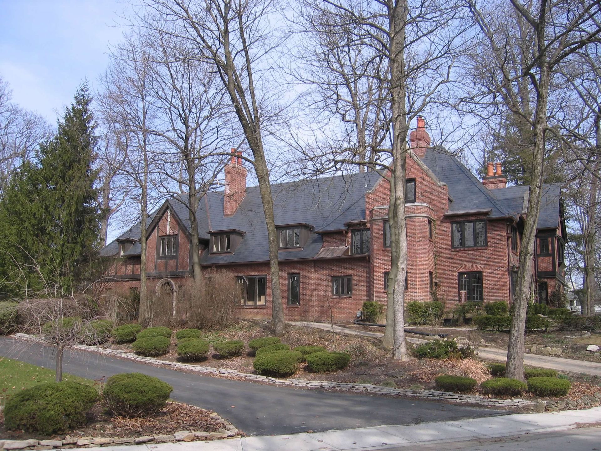A large brick house is surrounded by trees and bushes