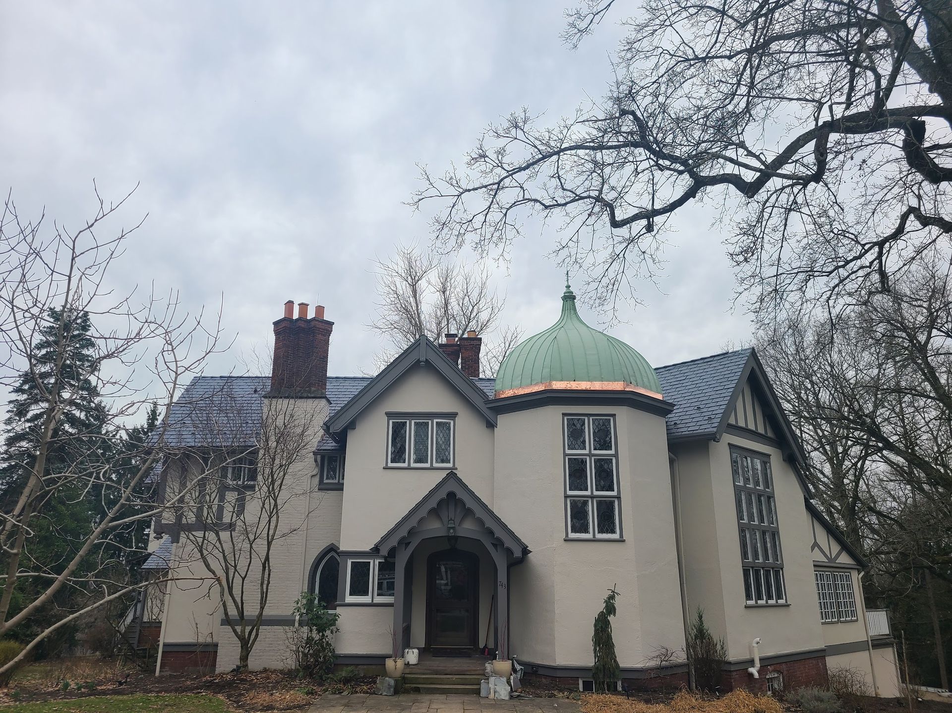 A large white house with a green roof is surrounded by trees on a cloudy day.