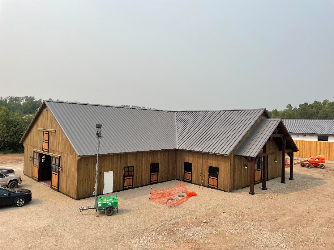 A large wooden barn with a metal roof is sitting in the middle of a dirt field.