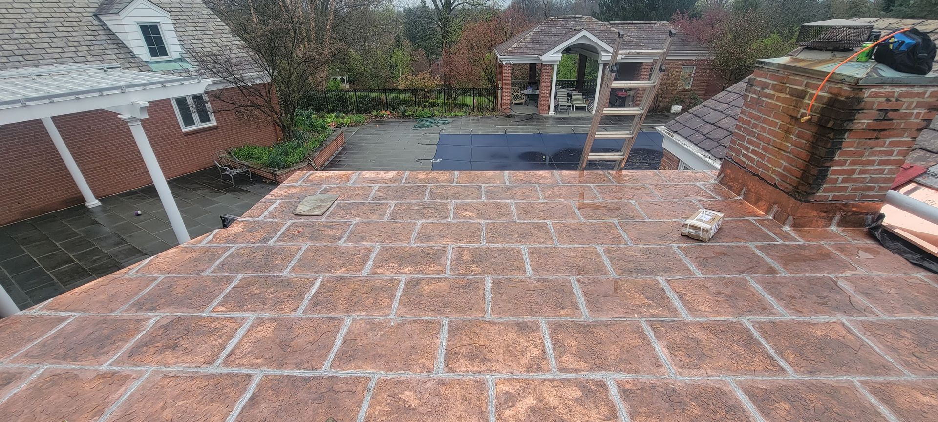 A brick roof with a ladder on it and a house in the background.