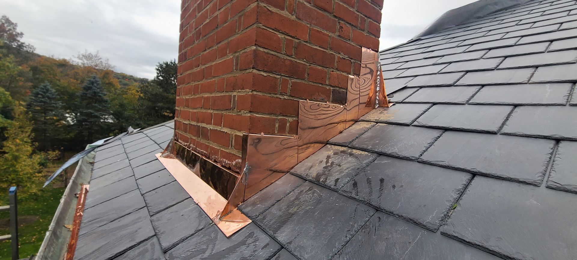 A brick chimney is sitting on top of a slate roof.