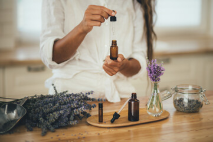 A person in a white shirt preparing lavender essential oil with amber glass bottles and fresh lavender on a wooden table.
