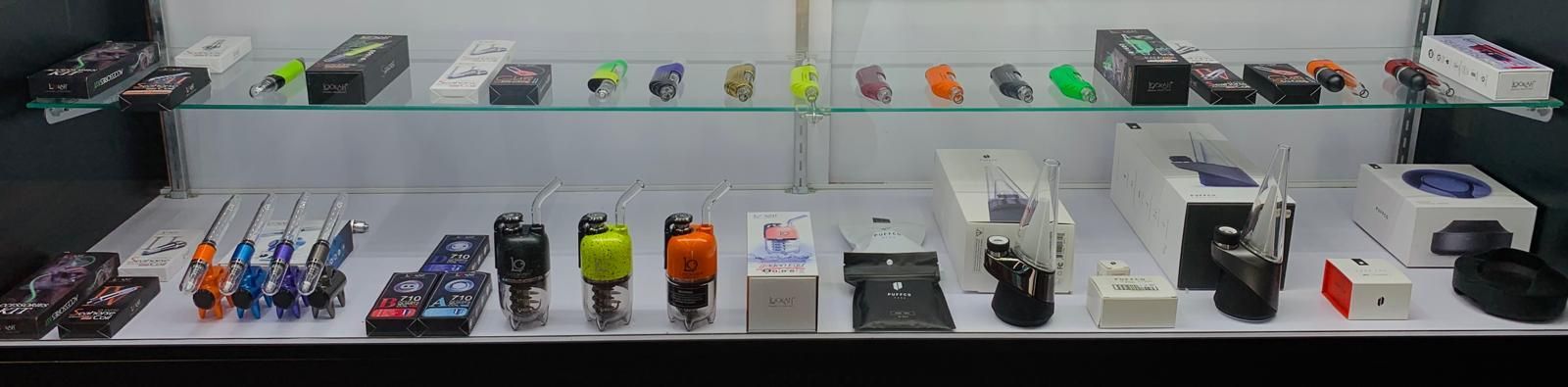 A brightly lit display shelf in a retail store showcasing various electronic cigarettes, accessories, and boxed products.