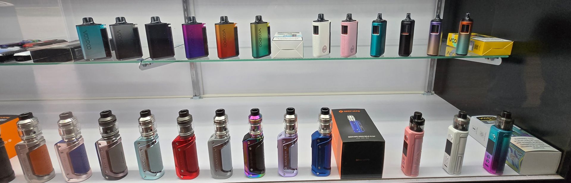 A store display featuring two shelves stocked with various colorful vape mods and tanks.