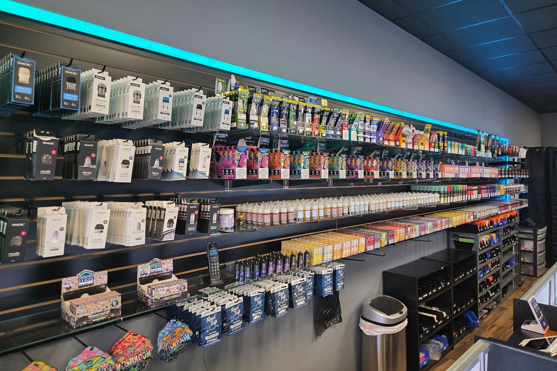 A retail wall featuring rows of vaping products and accessories, illuminated by a strip of bright blue LED lighting.