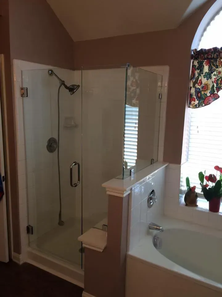 Glass shower enclosure in a bathroom with an adjacent bathtub near a window.
