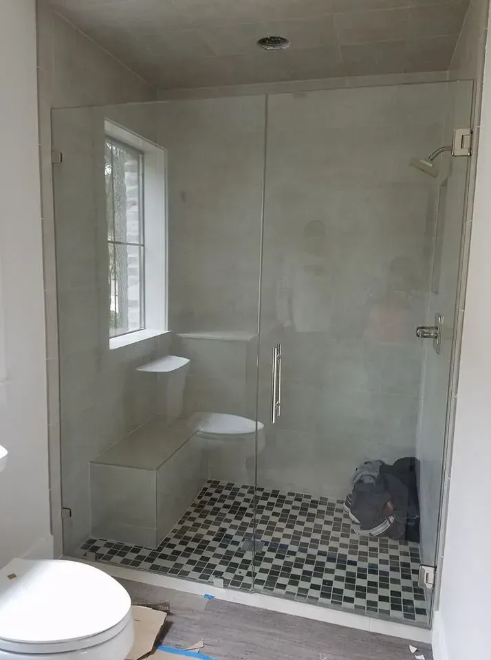 Glass shower enclosure with mosaic tile floor, toilet, and window.