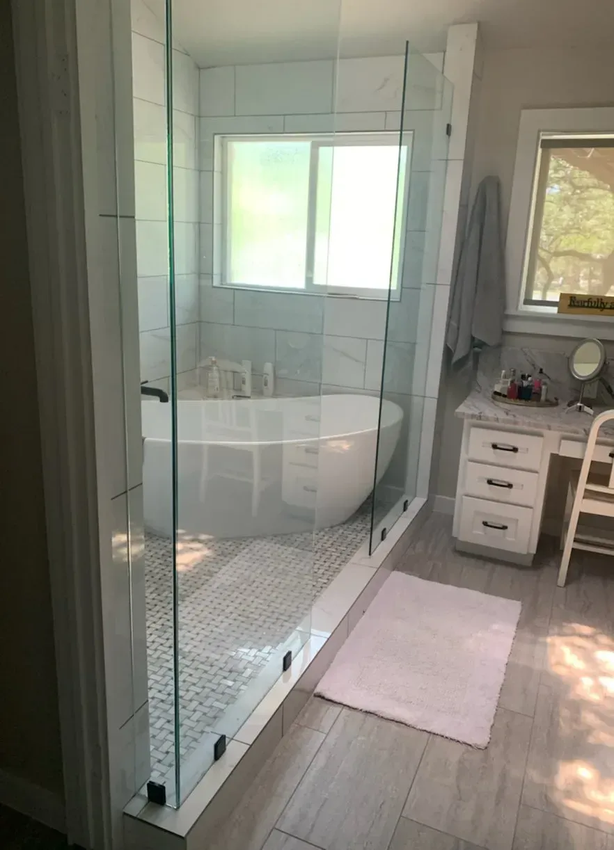 Modern bathroom with glass shower, tub, vanity, and light-colored tile.